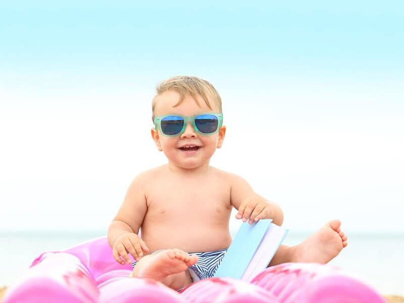 Un bébé avec des lunettes de soleil assis sur la plage