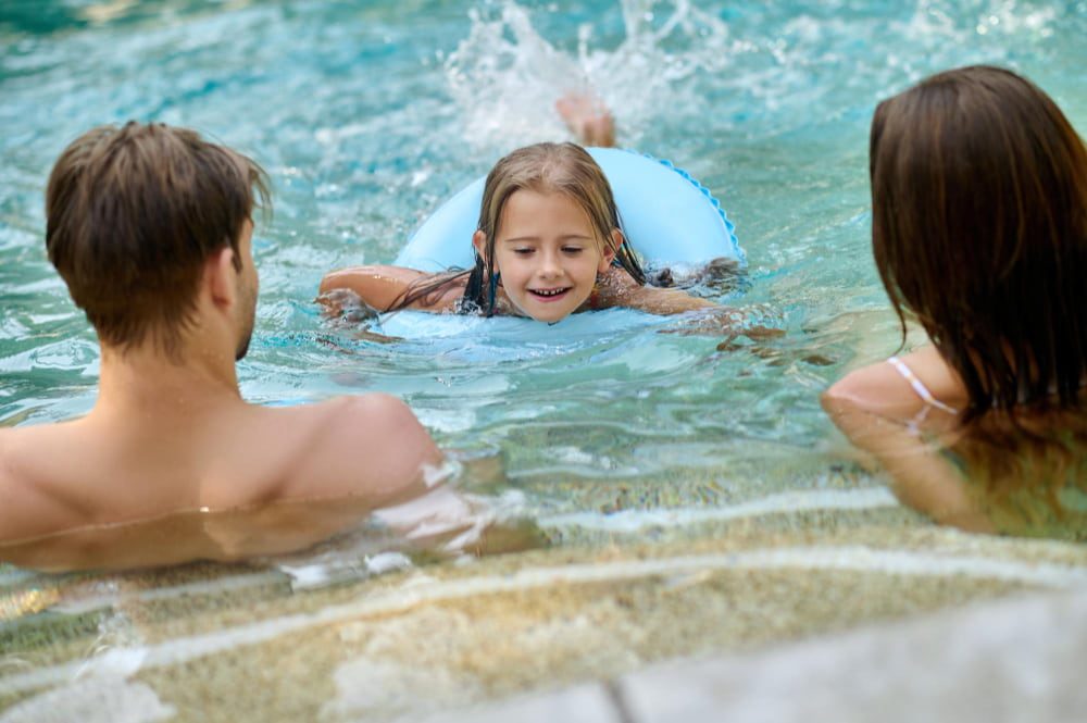 Comment respirer en nageant la brasse : une enfant nage avec ses parents dans une piscine