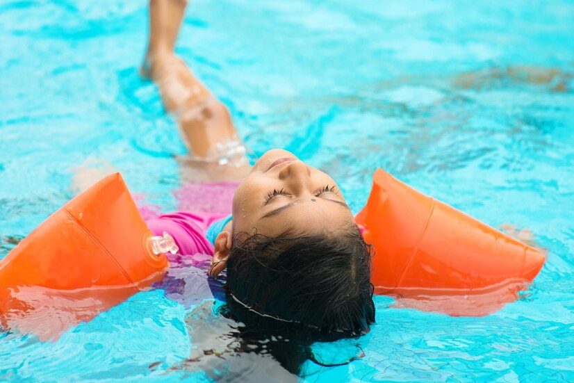 Une enfant flotte et apprend à s'allonger dans l'eau avec des brassards